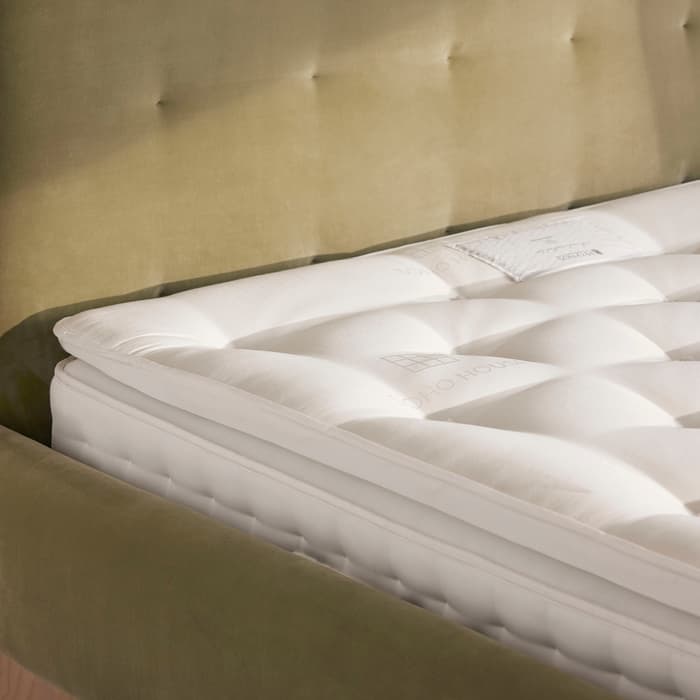 A white mattress with tufted detailing lies on a tufted olive-green bed frame. The mattress features SoHo House branding in an indoor bedroom setting with wood-panel flooring.